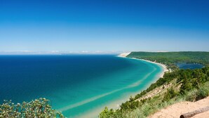 A coastal landscape with a clear view of the ocean, a sandy beach, and a forested area. - Lakeview Deck| 10 mi from TC | Sauna | Hot Tub (Traverse City)