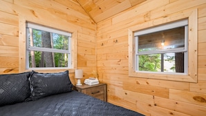 A wooden cabin room with a bed, two windows, and a nightstand with a lamp and towels. - Lakeview Deck| 10 mi from TC | Sauna | Hot Tub (Traverse City)
