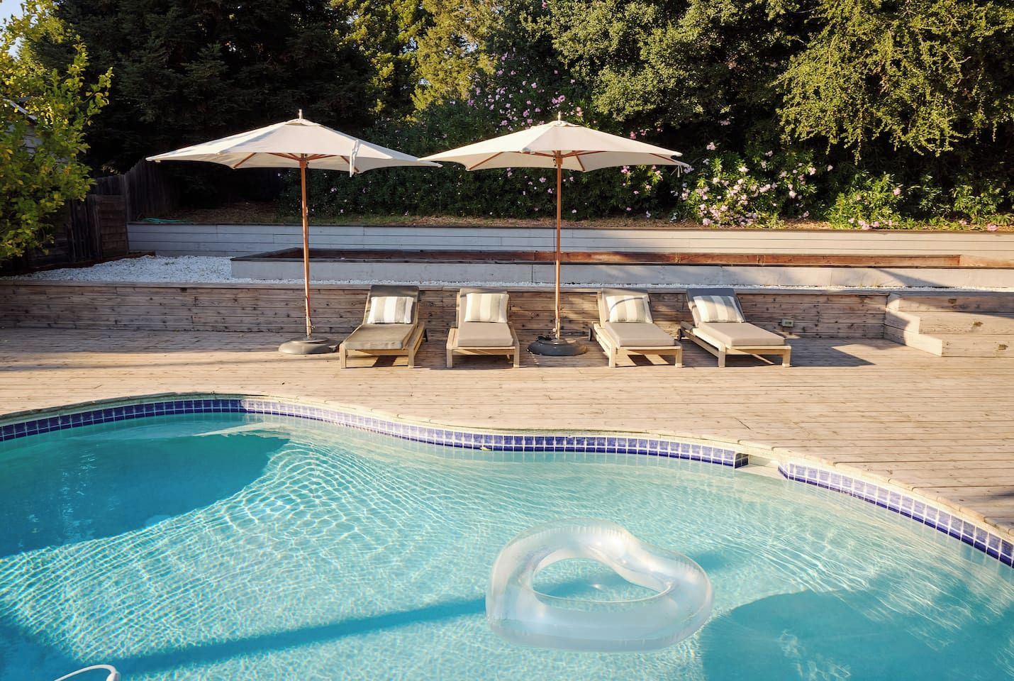 A swimming pool with clear blue water, surrounded by wooden deck and lounge chairs.