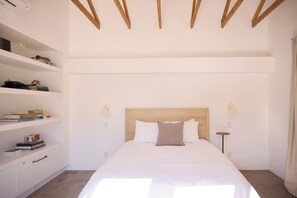 Un dormitorio minimalista con cabecera de madera, ropa de cama blanca y una mesita de noche con lámpara.