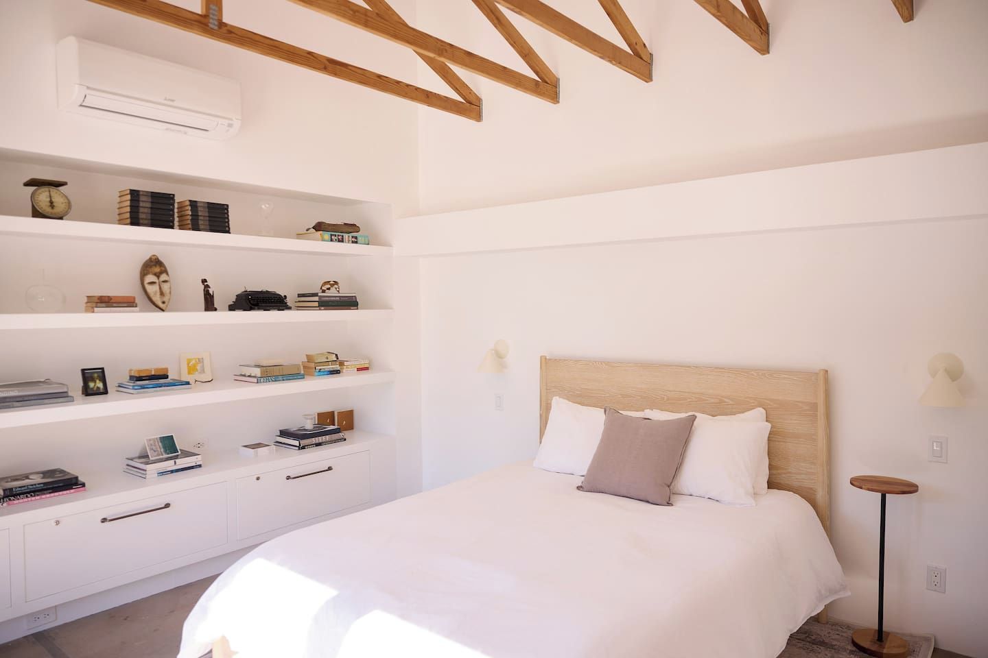Een slaapkamer met een bed, een witte kledingkast en een plank met boeken en decoratieve spullen.