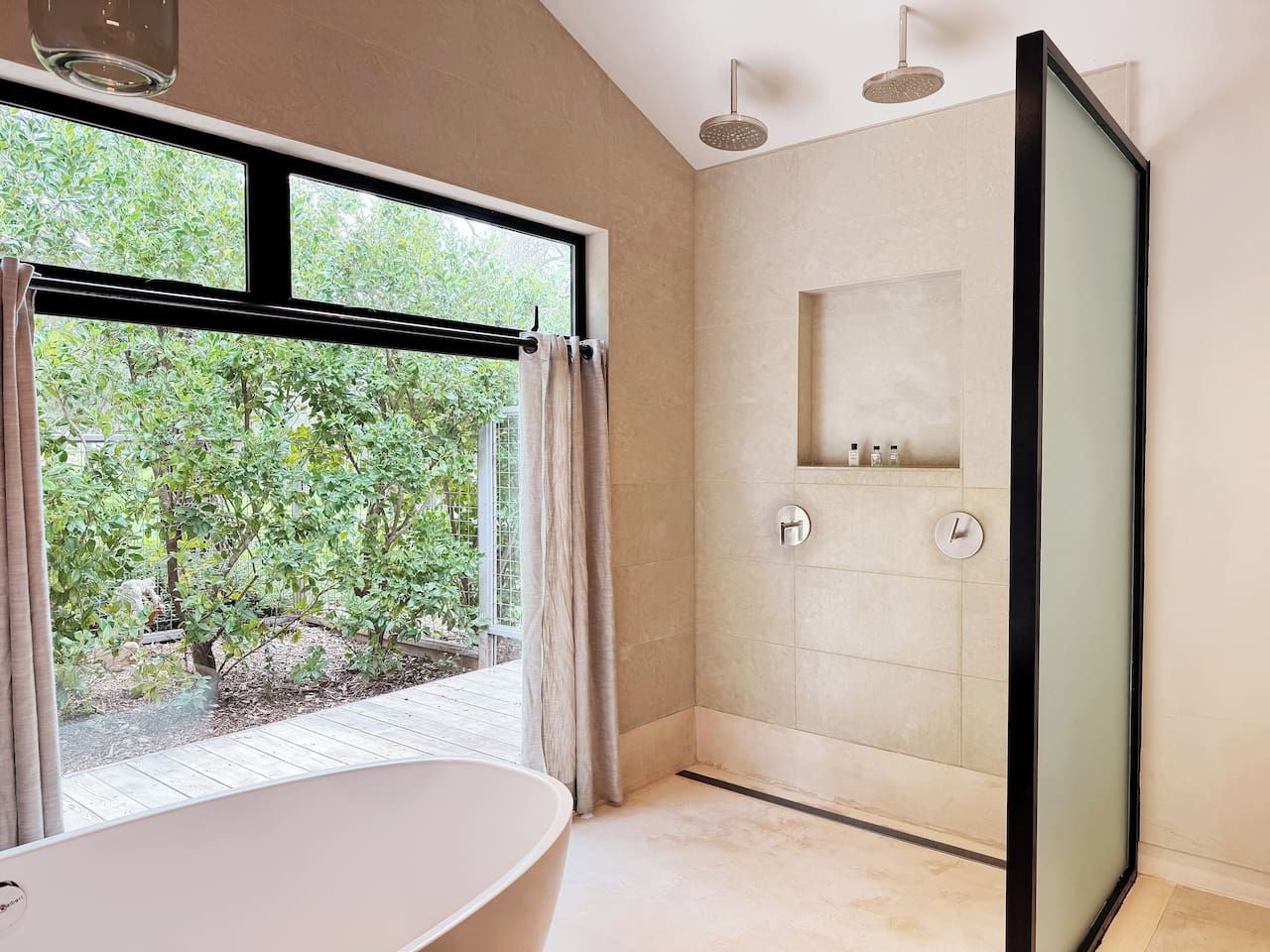 Un bagno moderno con una vasca freestanding, un box doccia in vetro e vista sul verde circostante.