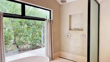 Un bagno moderno con una vasca freestanding, un box doccia in vetro e vista sul verde circostante.