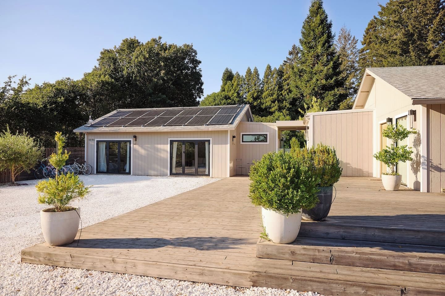 A modern house with a solar panel roof, a covered patio, and potted plants.