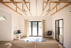 Una habitación con un sofá, una silla, una mesa con un ordenador portátil y un amplio ventanal con cortinas.