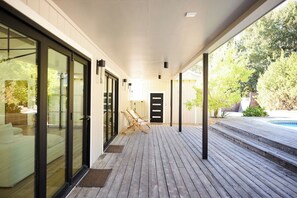 Un espacio al aire libre techado con piso de madera, puertas de vidrio y una piscina.