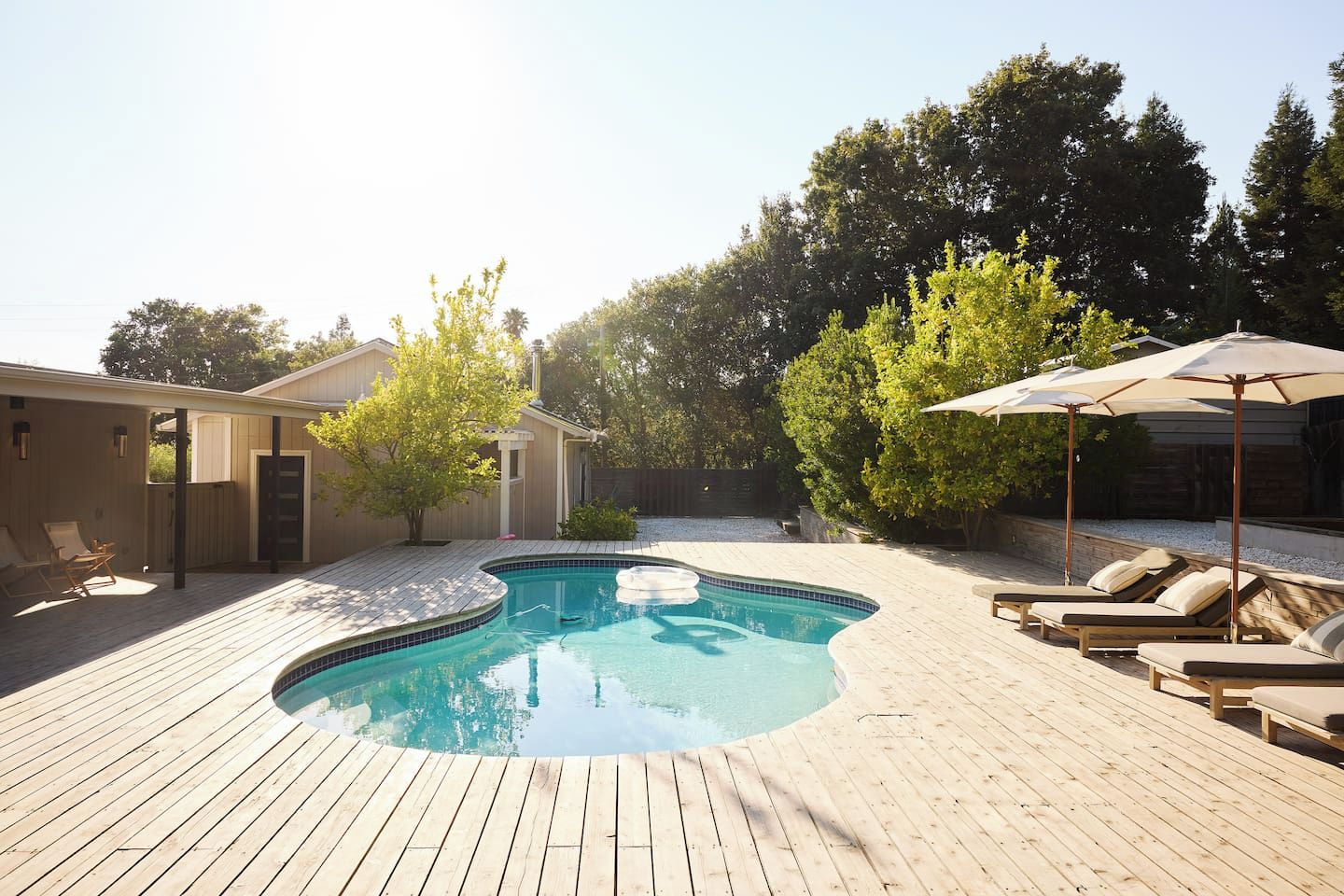 A wooden deck with a swimming pool, lounge chairs, and a covered area with umbrellas.
