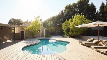 A wooden deck with a swimming pool, lounge chairs, and a covered area with umbrellas.
