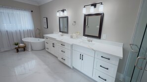 Ein modernes Badezimmer mit einer großen Badewanne, einem doppelten Waschbecken und einer Duschkabine aus Glas.
