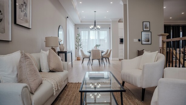 Een moderne woonkamer met een glazen salontafel, witte banken en een eethoek met een kroonluchter.