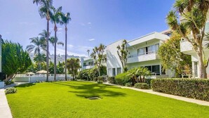 Un hotel moderno con césped cuidado, palmeras y un cielo azul despejado.
