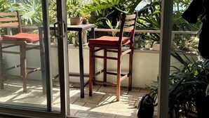 Una habitación con puerta corrediza de vidrio que da a un patio exterior. Hay una silla de madera con cojín rojo, una mesa y una planta en maceta.