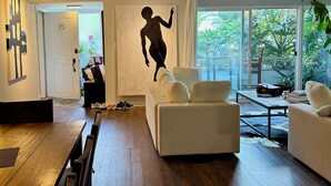 Una sala de estar moderna con un sofá blanco, una mesa de comedor de madera y un amplio ventanal con vistas a zonas verdes.