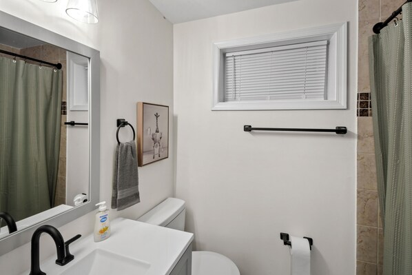 A bathroom with a white sink, black faucet, toilet, and a window with blinds. - Hilltop Retreat (Round Hill)