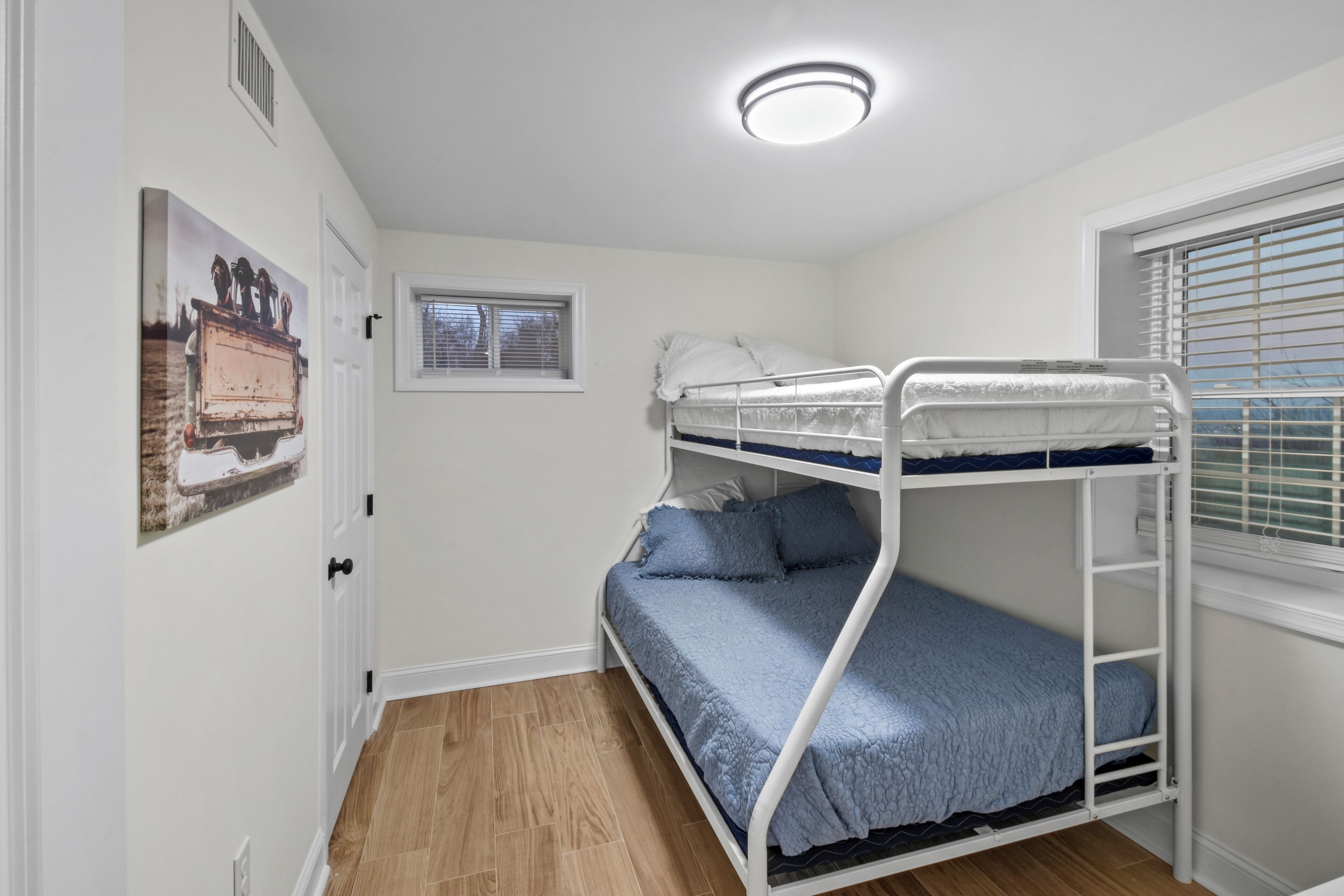 Een slaapkamer met stapelbed, raam, deur en een plafondlamp.