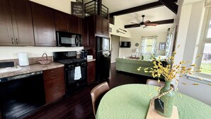 A modern kitchen with dark wood cabinets, a black stove, and a refrigerator. There is a dining area with a green table and a vase of flowers. - Discover the charm of Palmer Lake at this cozy cottage in this peaceful town. (Palmer Lake)
