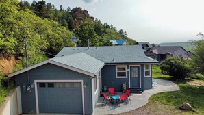 A two-story house with a garage, a patio with red and blue chairs, and a view of a forested hill. - Discover the charm of Palmer Lake at this cozy cottage in this peaceful town. (Palmer Lake)