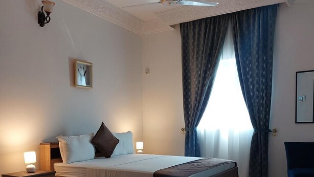 A well-lit bedroom with a large bed, a nightstand, a desk, and a chair.