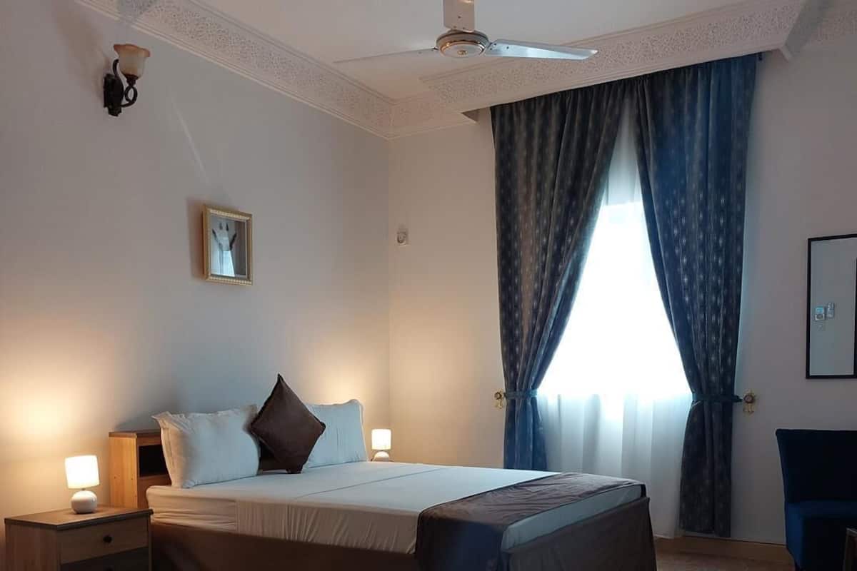 A well-lit bedroom with a large bed, a nightstand, a desk, and a chair.