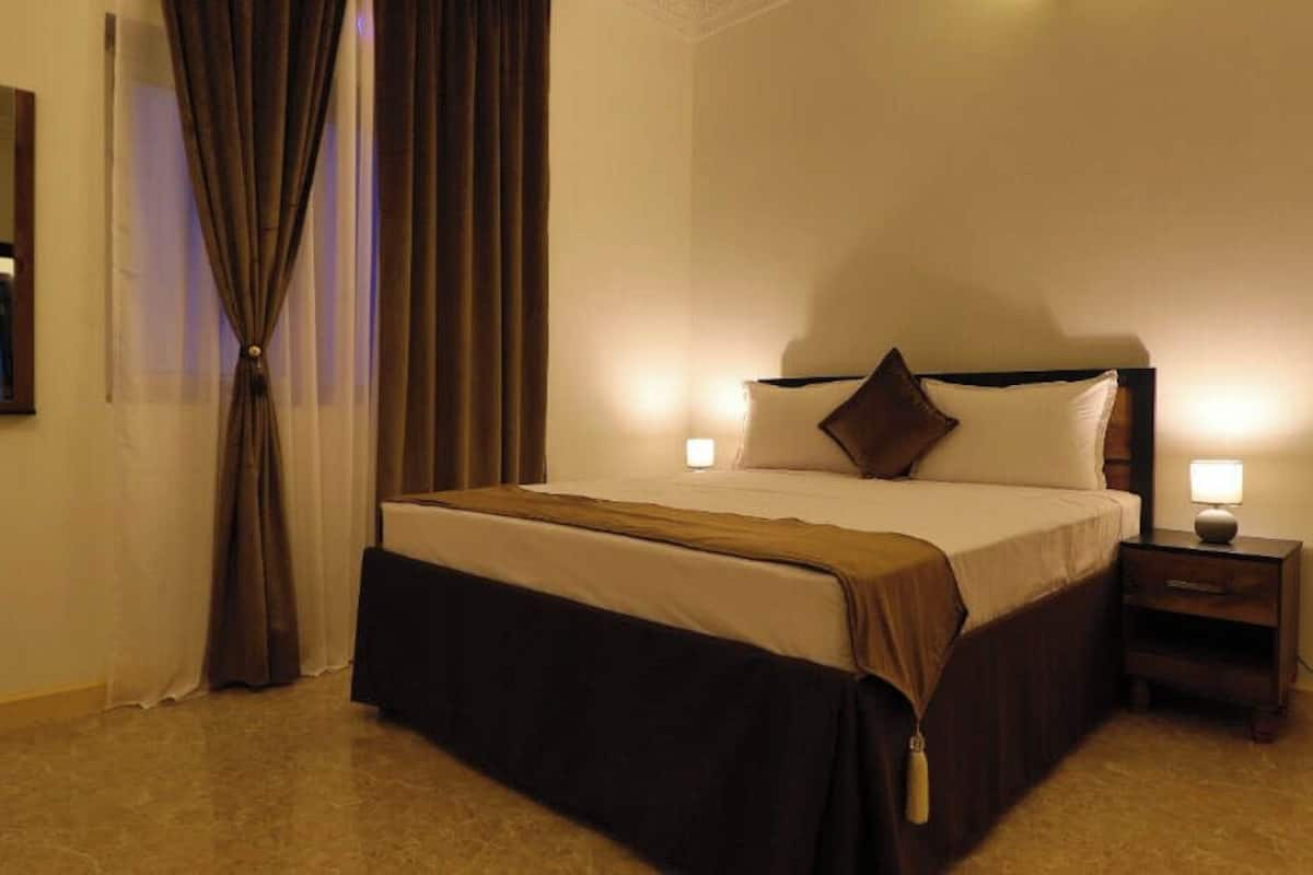 A hotel room with a bed, bedside table, and a mirror.