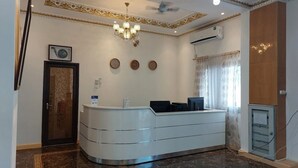 A reception area with a curved white desk, a chandelier, three wall clocks, and a door with a patterned glass panel.