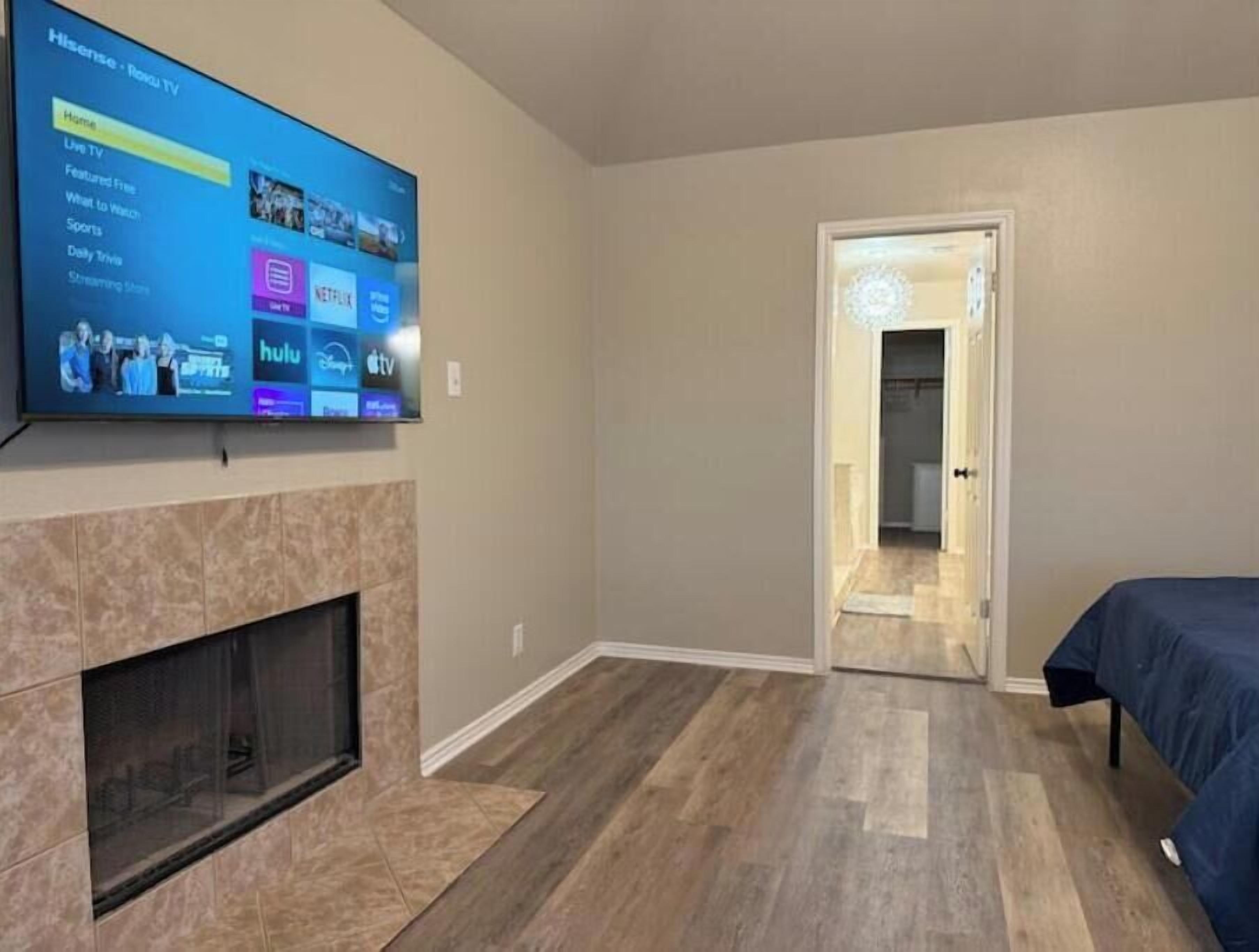 Una sala moderna con un televisor de pantalla plana montado en la pared, una chimenea y una puerta que da a otra habitación.