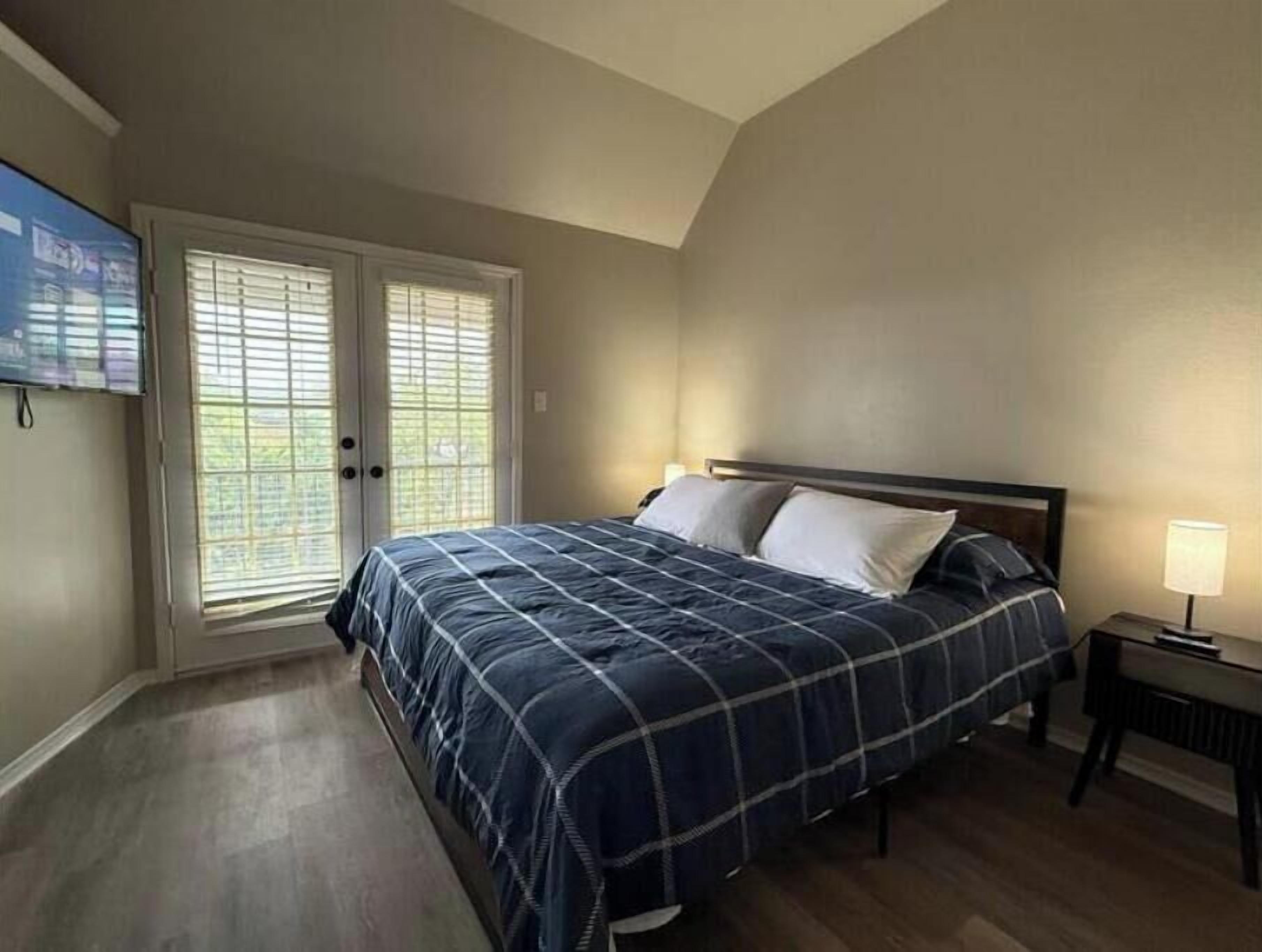 A bedroom with a bed, a nightstand, a TV, and a sliding glass door.