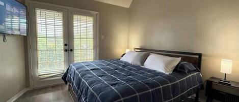 A bedroom with a bed, a nightstand, a TV, and a sliding glass door.