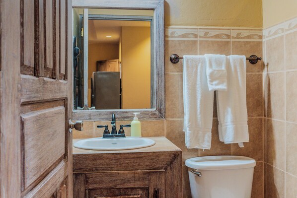 Un baño con tocador de madera, lavamanos, espejo, perchero para toallas y retrete.