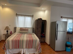 Un dormitorio con una cama, un armario de madera, un refrigerador, una lámpara y un dispensador de agua.