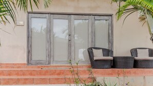 A building entrance with a glass door, a number plate '1B', and two wicker chairs with cushions on a tiled platform. - king Standart pool view (Tola)