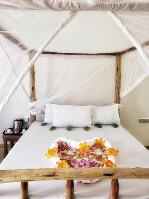 A bed with a white canopy and pillows, a wooden headboard, and a floral arrangement on the bed. - Serenity Boutique Hotel (Paje)