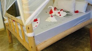Una cama de madera con dosel blanco, un colchón con inscripción de nombre y pétalos de rosa.