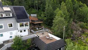 Ein Haus mit geneigtem Dach, Solaranlagen, einer Terrasse mit Sitzgelegenheiten und einer Steinmauer.