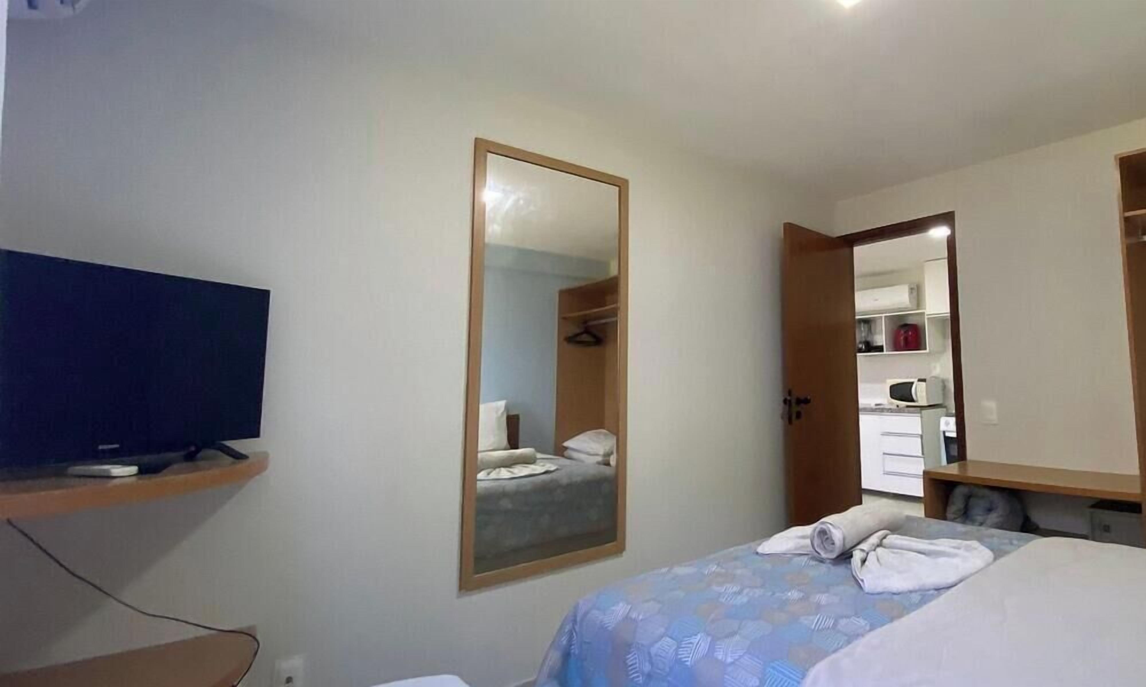 A hotel room with a bed, a television, a mirror, and a wardrobe.