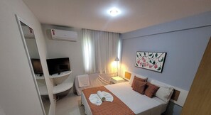 A hotel room with a bed, a desk, a television, and a painting on the wall. - Marupiara Suites (Ipojuca)
