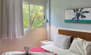 A hotel room with a bed, a nightstand, a lamp, a window with curtains, and a painting on the wall.