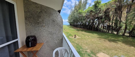 A balcony with a table and chairs, a speaker, and a view of a grassy area with trees.