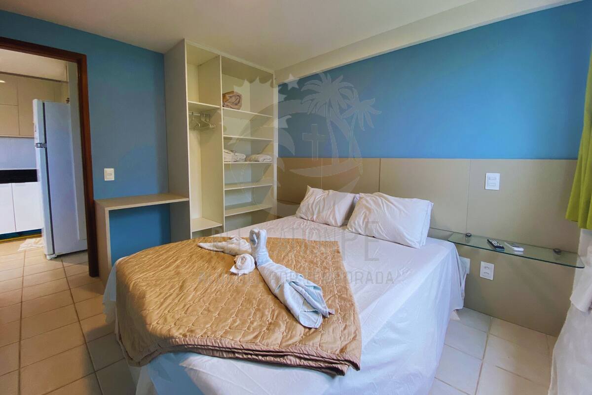 A hotel room with a bed, a wardrobe, a small table, and a wall with a palm tree mural.