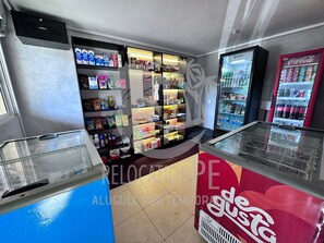 A room with a refrigerator, shelves stocked with beverages, and a Coca-Cola vending machine. - Marupiara Suites (Ipojuca)
