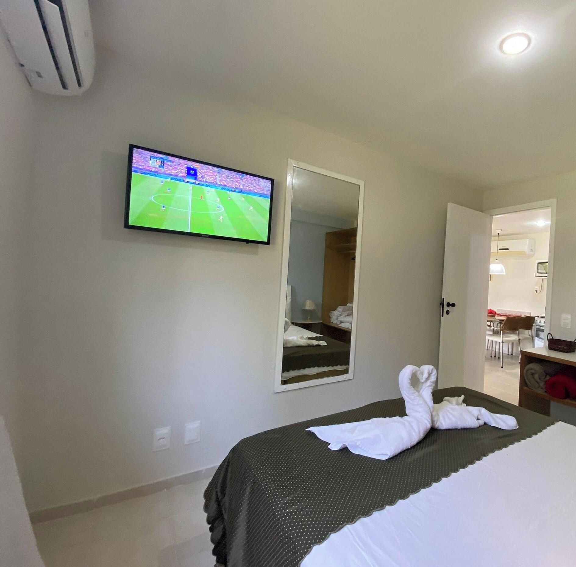 A hotel room with a bed, a television mounted on the wall, a mirror, and a door leading to a bathroom.