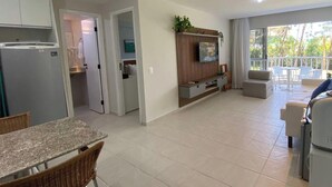 Una cocina moderna con refrigerador integrado, un comedor con mesa y sillas, una sala de estar con televisor de pantalla plana y un balcón con mobiliario exterior.