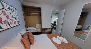 A hotel room with a bed, a wooden wardrobe, a mirror, and a painting on the wall. - Marupiara Suites (Ipojuca)