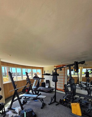 A gym with various exercise equipment, large windows, and a view of the outdoors.