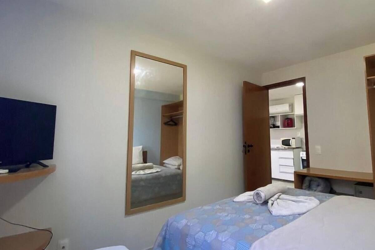 A hotel room with a bed, a television on a stand, a mirror, and a wardrobe.