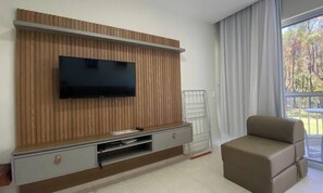 Ein modernes Wohnzimmer mit einem Flachbildfernseher an einer Holzwand, einer Couch und einem Fenster mit Vorhängen.