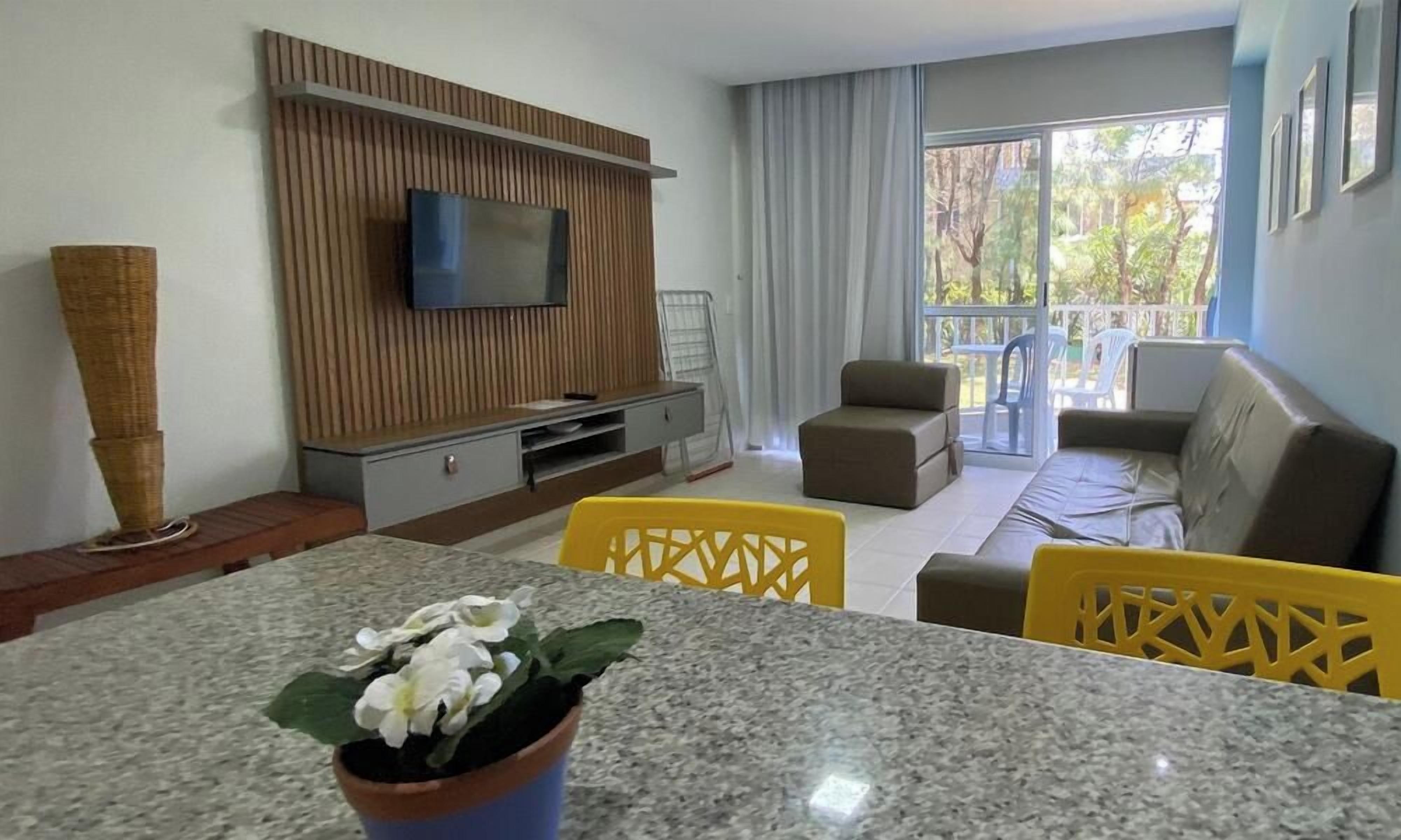 Una sala de estar moderna con un televisor de pantalla plana, un sofá, una mesa de comedor con sillas y un balcón con mobiliario exterior.