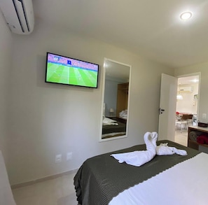 A hotel room with a bed, a TV mounted on the wall, a mirror, and a bathroom visible through an open door.