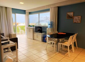 A compact living space with a balcony, a kitchenette, a dining area, and a TV. - Marupiara Suites (Ipojuca)