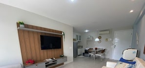 A living room with a TV, dining table, chairs, and a sofa.